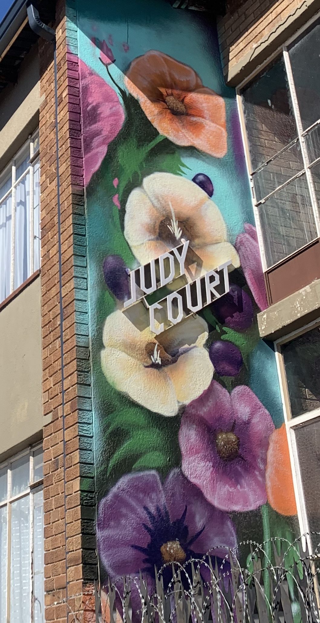 Floral mural reading Judy Court painted across an apartment-block wall